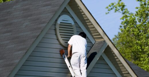 Painter working at the top of an extension ladder on a two story suburban home.
